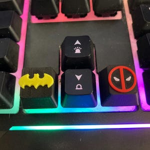 Teclas inspiradas en superhéroes con figuras de Batman y Deadpool.