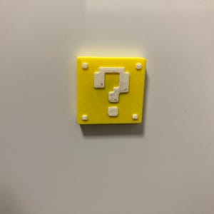 May include: A square yellow magnet featuring a white pixelated question mark in the centre and four small white squares in each corner. The design mimics a classic video game block, providing a bright and recognisable decorative accent piece.