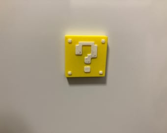 May include: A square yellow magnet featuring a white pixelated question mark in the center and four small white squares in each corner. The design mimics a classic video game block, providing a bright and recognizable decorative accent piece.