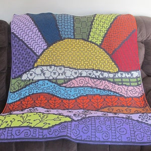 Könnte beinhalten: Eine bunte gehäkelte Decke mit einem Sonnenaufgangsmuster. Die Decke zeigt eine gelbe Sonne, blaue und grüne Hügel und rote und orange Blätter. Die Decke ist aus verschiedenen farbigen Quadraten gefertigt und eine großartige Ergänzung für jedes Zuhause.