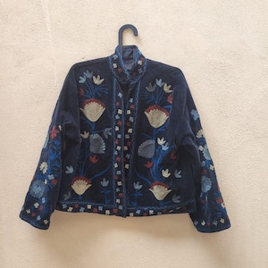 May include: A dark blue velvet jacket featuring intricate floral embroidery in shades of blue, red, and white. The jacket has a high collar and long sleeves.