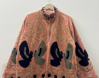 May include: A peach-colored jacket featuring dark navy and muted green embroidered bird motifs. The garment includes intricate gold-toned swirling vine embroidery across the front and sleeves, with a high collar and a front opening design.