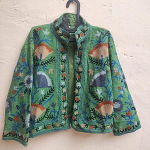 May include: A green embroidered jacket with floral and geometric patterns in shades of blue, orange, and brown. The jacket has a mandarin collar and long sleeves.