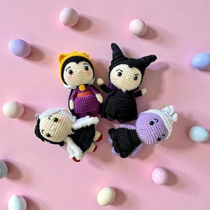 May include: Four crocheted dolls of Disney villains, including the Evil Queen, Maleficent, Cruella de Vil, and Ursula, are arranged on a pink background. The dolls are in their signature outfits, with details like hats and capes. Pastel-colored eggs are scattered around the dolls.