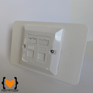 Może przedstawiać: Biała płyta ścienna z czterema portami danych oznaczonymi "DATA" i "CAT6". Płyta jest prostokątna z zaokrąglonymi narożnikami i jest zamontowana na białej ścianie. Logo "FOXTRTCOM" jest widoczne na dole.