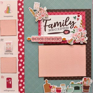 May include: A scrapbook page with a teal and pink color scheme, featuring the words "Family Recipes" and "What's Cookin?" Decorative elements include floral accents, a rolling pin, and illustrations of kitchen tools and food items like a flour bag and refrigerator.