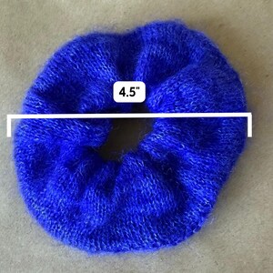 May include: A vibrant royal blue fuzzy hair scrunchie with a soft, textured knit appearance. A white graphic overlay indicates a diameter of 4.5 inches, clearly marking the size of this circular hair accessory against a neutral background.