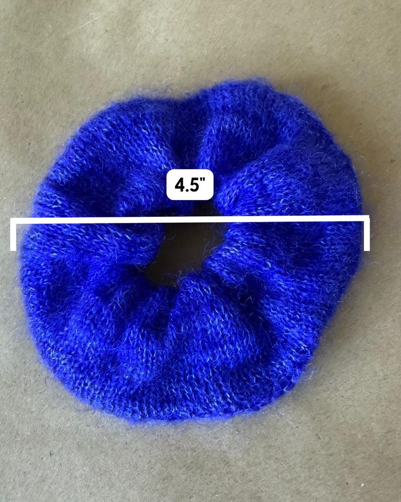 May include: A vibrant royal blue fuzzy hair scrunchie with a soft, textured knit appearance. A white graphic overlay indicates a diameter of 4.5 inches, clearly marking the size of this circular hair accessory against a neutral background.
