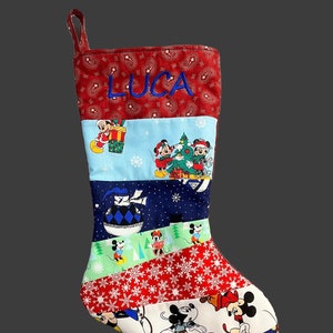 May include: A red, blue, and green Christmas stocking with a patchwork design featuring Mickey Mouse characters. The stocking has a loop at the top and is personalized with the name "LUCA".