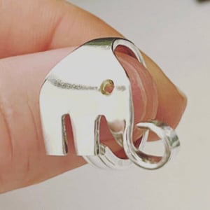 May include: A silver ring shaped like an elephant. The elephant's body is hollow and the ring is worn on a finger.