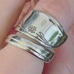 K&ouml;nnte beinhalten: Ein silberner L&ouml;ffelring mit einem floralen Design und einem vierbl&auml;ttrigen Kleeblatt, das in die Band graviert ist.