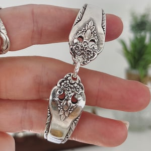 May include: A silver bracelet made from two vintage spoons, connected by a chain. The spoons have ornate floral designs and are joined together at the top.