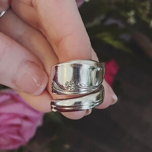 K&ouml;nnte beinhalten: Ein silberner L&ouml;ffelring mit einem Blumendesign. Der Ring besteht aus zwei L&ouml;ffeln, die umeinander gewickelt sind.