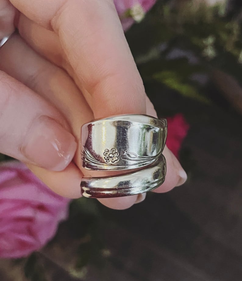 K&ouml;nnte beinhalten: Ein silberner L&ouml;ffelring mit einem Blumendesign. Der Ring besteht aus zwei L&ouml;ffeln, die umeinander gewickelt sind.