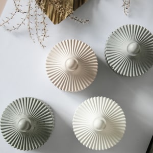 Puede incluir: Cuatro portavelas decorativos de hormigón con forma de pequeña estructura redonda y abovedada con un diseño acanalado. Los portavelas son de color blanco, gris y rosa.