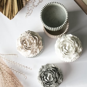 Op de afbeelding: Drie decoratieve betonnen bloemvormige dozen met deksels. De dozen zijn in grijstinten en wit.