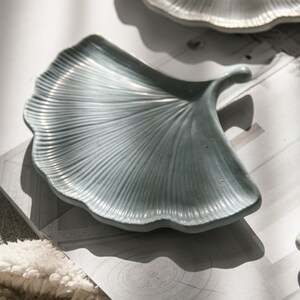 May include: A set of three ceramic dishes shaped like ginkgo leaves. The dishes are in shades of grey and white.