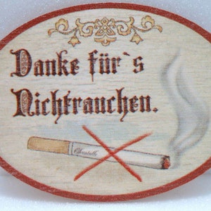 May include: Oval wooden sign with the German text "Danke für's Nichtrauchen" and a crossed-out cigarette illustration. The sign has a light wood grain background with a red border and decorative flourishes.