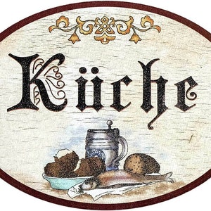 May include: A wooden oval sign with a red border and the word "Küche" in black script. The sign features a painted illustration of a beer stein, bread, potatoes, and a fish.