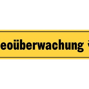 Könnte beinhalten: Ein gelbes Schild mit schwarzem Text und einer schwarzen Silhouette einer Überwachungskamera. Das Schild lautet "Videoüberwachung".