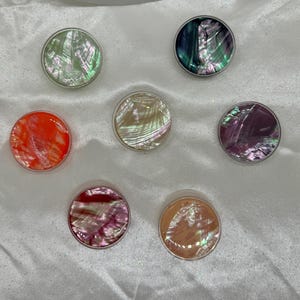 May include: Seven round phone grips with iridescent mother of pearl designs. The grips are in various colors including green, orange, pink, and white.