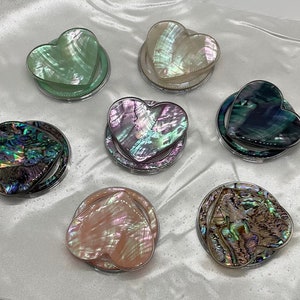 May include: Six heart-shaped iridescent mother-of-pearl phone grips with silver rings. The grips are in various colors, including green, white, pink, blue, and brown.