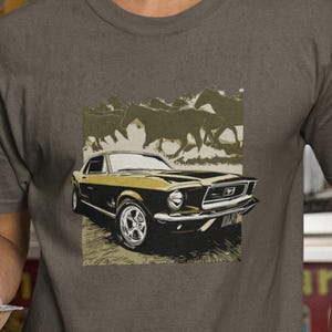 May include: Dark gray t-shirt featuring a vintage car with a yellow top and black body. The graphic includes a background of running horses. The shirt is a classic crew neck style.