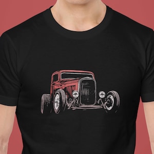 Könnte beinhalten: Schwarzes T-Shirt mit einer roten Grafik eines Oldtimer-Hot-Rod-Autos. Das Autodesign umfasst große Reifen und Scheinwerfer. Die Grafik ist mittig auf dem T-Shirt platziert und bietet ein auffälliges Design.