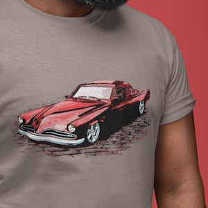 May include: A red vintage car with chrome accents on a gray t-shirt. The car has a rounded body style and a single headlight on each side.