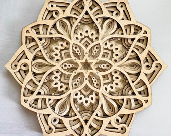 Könnte beinhalten: Ein lasergeschnittenes Holzmandala mit filigranen Details und einem geschichteten Design. Das Mandala ist aus hellbraunem Holz gefertigt und hat eine kreisförmige Form.