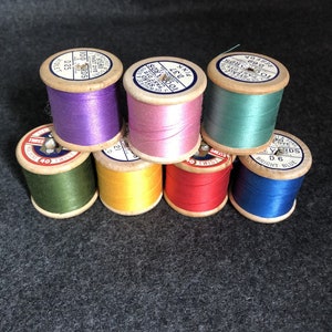 May include: Eight spools of thread in various colours, including purple, pink, teal, green, yellow, red, and blue. Each spool has a label with the text "100 YARDS" and the colour name. The spools are arranged in a pyramid shape.