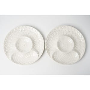 May include: Two round white ceramic serving platters featuring a central circular bowl and a separate oval-shaped compartment. The surface of each platter is decorated with a textured leaf pattern radiating from the center and a cross-hatch design.