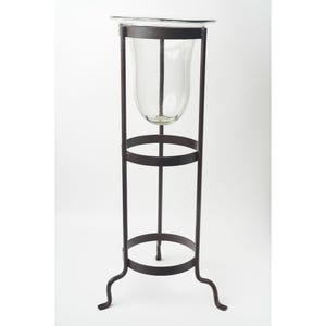 May include: A tall, wrought iron plant stand with a clear glass vase. The stand has a dark brown finish, with a circular base and a flared, three-legged base. The glass vase is a bulbous shape, perfect for displaying flowers or greenery.