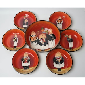Può includere: Un set di sette piatti in ceramica con interno rosso e bordo nero. Ogni piatto presenta un design a cartone animato di un cameriere in smoking, che tiene in mano vari oggetti come bottiglie di vino e cibo. I piatti sono disposti su una superficie bianca.