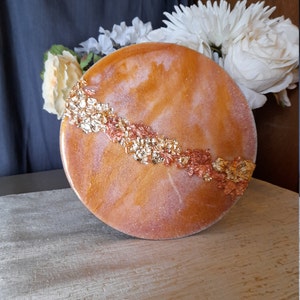 May include: A round, orange and white resin art piece with gold and copper flakes embedded in the resin.