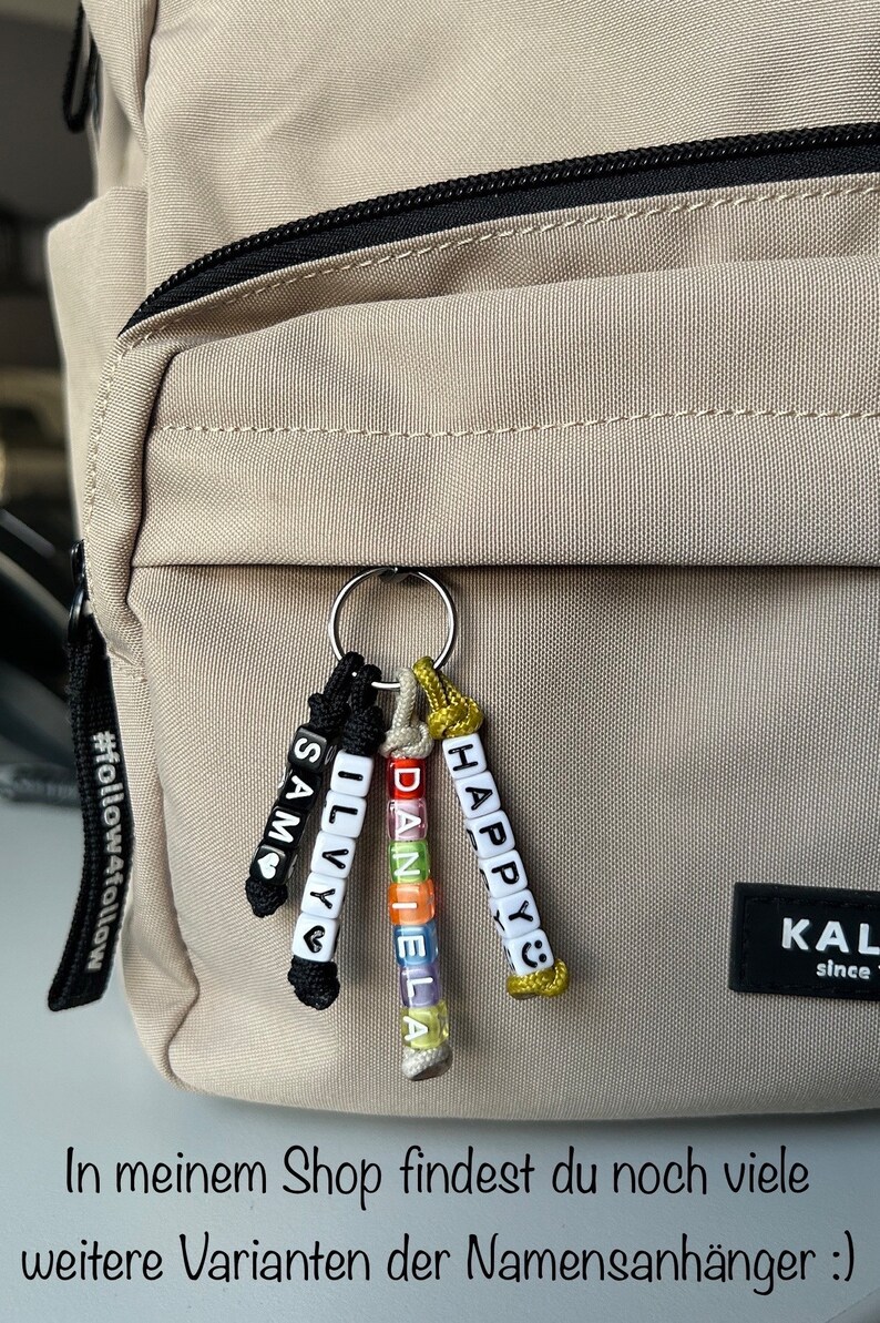 May include: A keychain with personalized name beads attached to a beige backpack. The keychain features the names "SAM", "ILVY", "DANIELA", and "HAPPY" spelled out with colorful letter beads. The text "In meinem Shop findest du noch viele weitere Varianten der Namensanh&auml;nger :)" is visible.