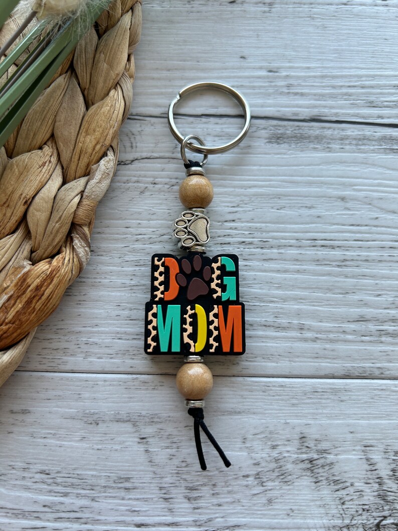 May include: A black and colourful keychain with the words "Dog Mom" and a paw print. The keychain has wooden beads and a silver key ring.