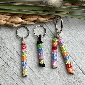 May include: Three keychains with names spelled out in colorful letter beads. The names are "DANIELA", "FELIX", and "FRANZISKA". Each keychain has a silver ring and a cord or string to hold the beads.