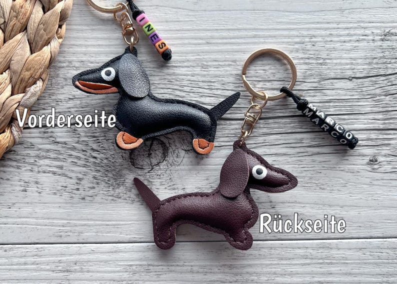 May include: Two dachshund keychains. One is black with orange paws, the other is brown. Each has a gold keyring and a small beaded name tag. The black keychain has the name "INES" and the brown keychain has the name "MARCO".