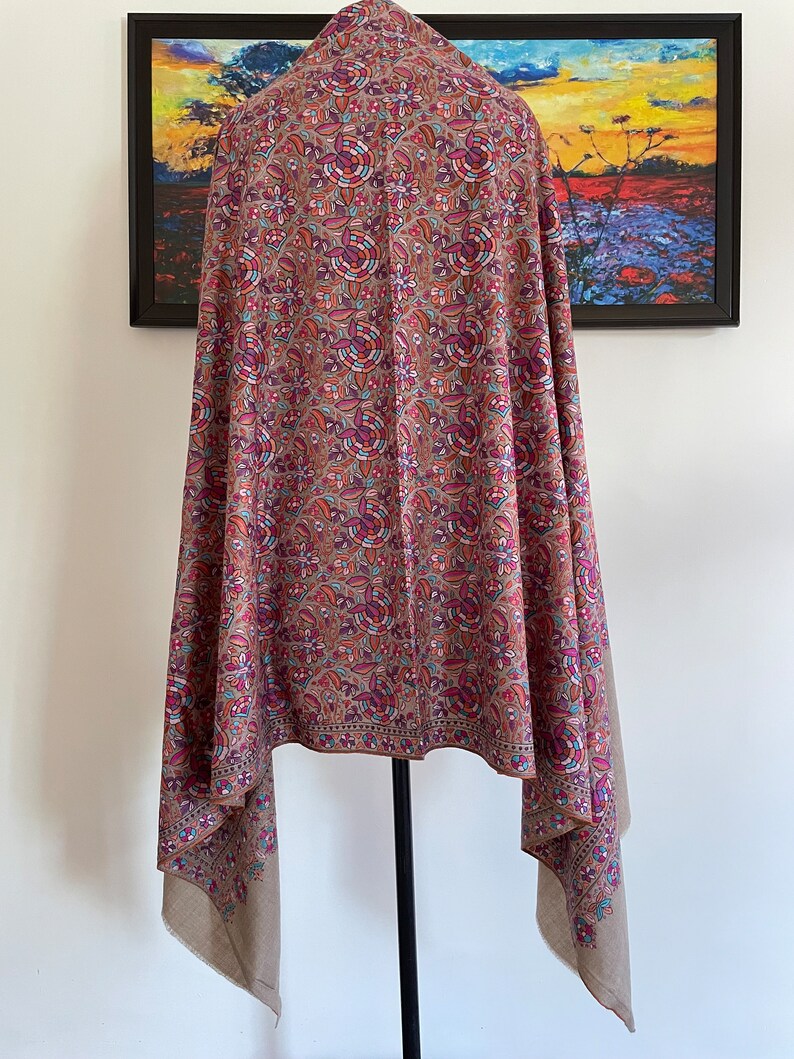 May include: A brown shawl with a floral pattern in shades of pink, blue, and orange. The shawl is made of a soft, lightweight fabric and has a fringed edge.