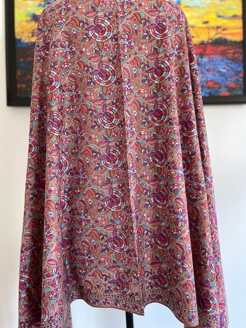 May include: A brown shawl with a floral pattern in shades of pink, blue, and orange. The shawl has a decorative border.