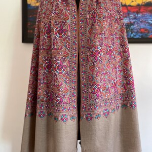 May include: A brown shawl with a floral pattern in shades of pink, purple, blue, and orange. The shawl has a fringed edge and is made of a soft, luxurious fabric.