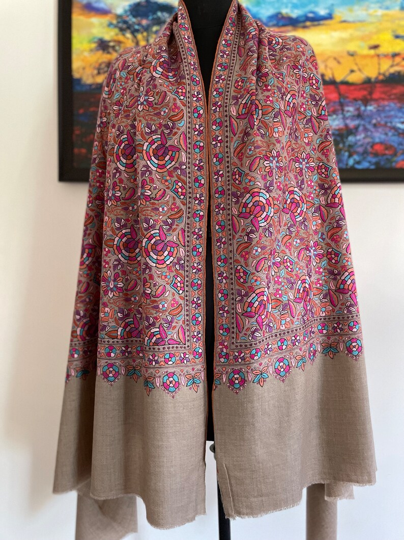 May include: A brown shawl with a floral pattern in shades of pink, purple, blue, and orange. The shawl has a fringed edge and is made of a soft, luxurious fabric.