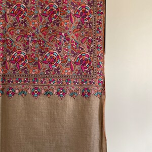 May include: A brown shawl with a colorful floral pattern. The shawl has a fringe border and is made of a soft, luxurious fabric.