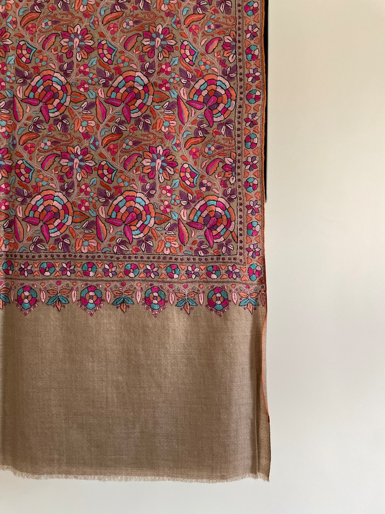 May include: A brown shawl with a colorful floral pattern. The shawl has a fringe border and is made of a soft, luxurious fabric.
