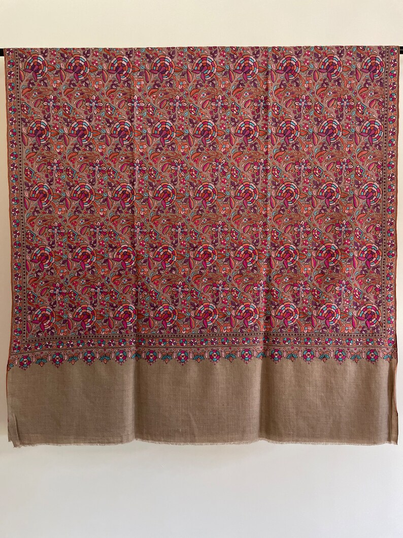 May include: A brown shawl with a floral pattern in shades of pink, red, blue, and green. The shawl has a solid brown border.
