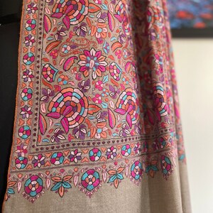 May include: A brown shawl with intricate floral embroidery in shades of pink, blue, and orange. The shawl has a border of smaller floral designs.