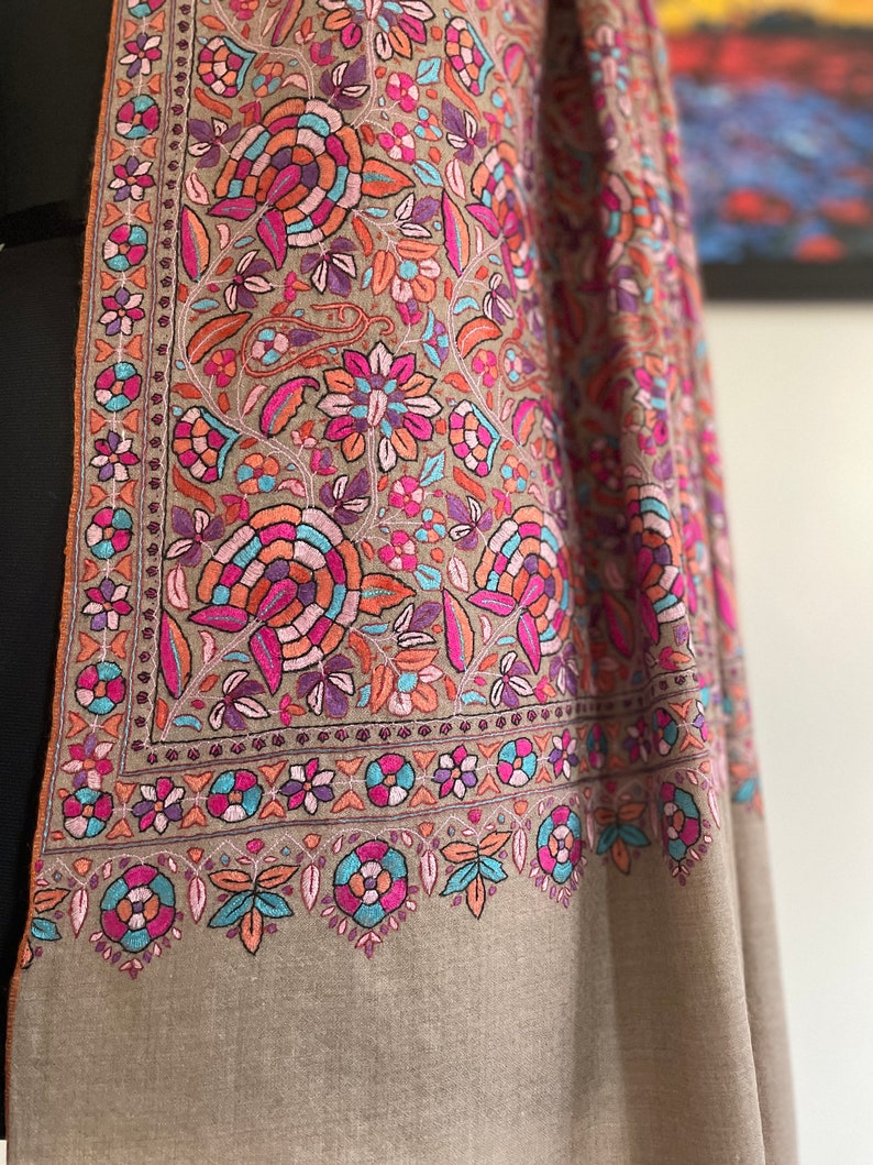 May include: A brown shawl with intricate floral embroidery in shades of pink, blue, and orange. The shawl has a border of smaller floral designs.