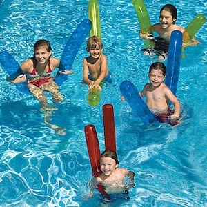 May include: A group of children in a swimming pool, using colourful foam pool noodles. The noodles are blue, green, and red. The children are smiling and having fun in the water. The water is a bright, clear blue.