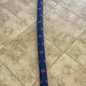 May include: A navy blue, cylindrical case with a repeating pattern of red "B" logos, possibly for a baseball bat or sports equipment. It has a white drawstring closure at the top.